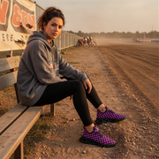Woman sitting on a wooden bench at a race track wearing checkered boots.