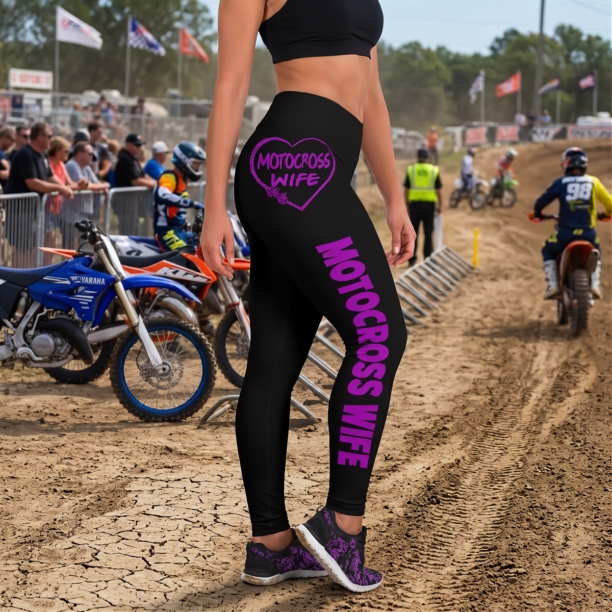 Black athletic leggings with purple 'MOTOCROSS WIFE' text and a heart graphic, worn by a model on a dirt motocross track.