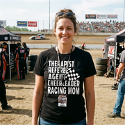 Premium black women's t-shirt mockup featuring a clean white graphic layout listing "THERAPIST REFEREE AGENT CHEERLEADER RACING MOM" paired with a classic checkered flag icon.
