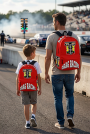 An adult man and an 8 to 12 year old child walking side by side down a drag strip lane toward the staging lights, both wearing identical custom red drag racing track backpacks viewed from behind.