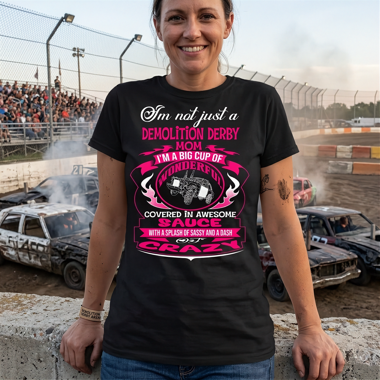 Premium women's black graphic t-shirt mockup featuring a vibrant pink and white custom design that reads "I'm not just a Demolition Derby Mom, I'm a big cup of wonderful covered in awesome sauce with a splash of sassy and a dash of crazy" with a derby car illustration.