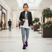 Woman walking in a shopping mall wearing a black jacket, white shirt, blue jeans, and purple shoes.