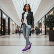 Woman in a black leather jacket, white shirt, and ripped jeans with purple sneakers in a mall.