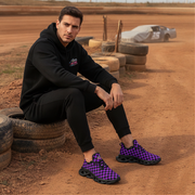 Man sitting on a tire with checkered purple and black shoes in a dirt track setting