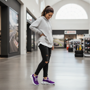 Woman wearing a gray hoodie, black ripped jeans, and purple sneakers in a store.