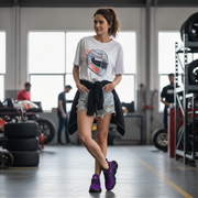 Woman in a garage wearing a graphic t-shirt and purple sneakers.