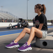 Woman sitting on a track wearing purple checkered sneakers with a race car in the background.