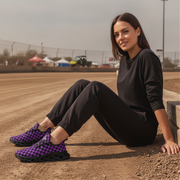 Woman sitting on a dirt track wearing black and purple checkered shoes