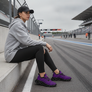 woman sitting on a race track wearing gray hoodie, black leggings, and purple checkered shoes.
