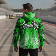 A man stands on a racetrack wearing a bright green hoodie from the back, featuring a large 'Racing' graphic with checkered flags and white tire tracks.