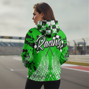 A woman stands on a racetrack wearing a bright green hoodie with a black and white checkered hood, black splatter graphics, and a large 'Racing' graphic with tire tracks on the back.