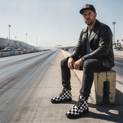 Man sitting on a concrete block on a race track wearing checkered boots.