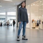 Woman wearing a gray sweater, blue jeans, and checkered boots in a modern indoor setting.