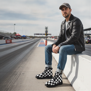 Man sitting on a race track wearing checkered boots and a leather jacket.