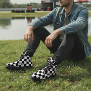 Man wearing checkered boots sitting on grass near a lake