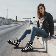 Woman sitting on a concrete barrier at a race track wearing checkered boots.