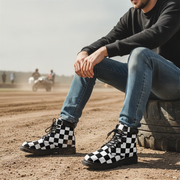 Man wearing checkered boots sitting on a tire with a dirt track background