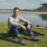 Man sitting on grass by a lake with checkered boots