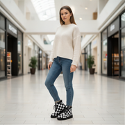 Woman wearing a white sweater, blue jeans, and checkered boots in a shopping mall.
