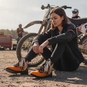 Woman sitting on a dirt track next to a bike wearing a checkered pattern orange boots
