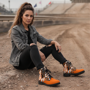 Woman in athletic wear standing on a race track wearing orange checkered dirty boots with a car in the background 
