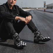 Man sitting on a road wearing black and white checkered shoes and socks.
