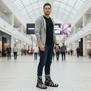 Man standing in a modern mall wearing a gray cardigan, black shirt, blue jeans, and checkered boots.