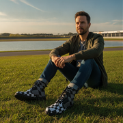 Man sitting on grass wearing checkered boots with a lake and sky in the background