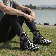 Person wearing black and white checkered boots sitting on grass with a lake in the background