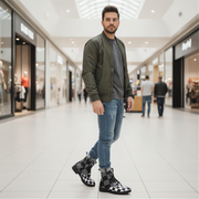 Man wearing a green jacket, gray shirt, blue jeans, and checkered boots in a shopping mall.
