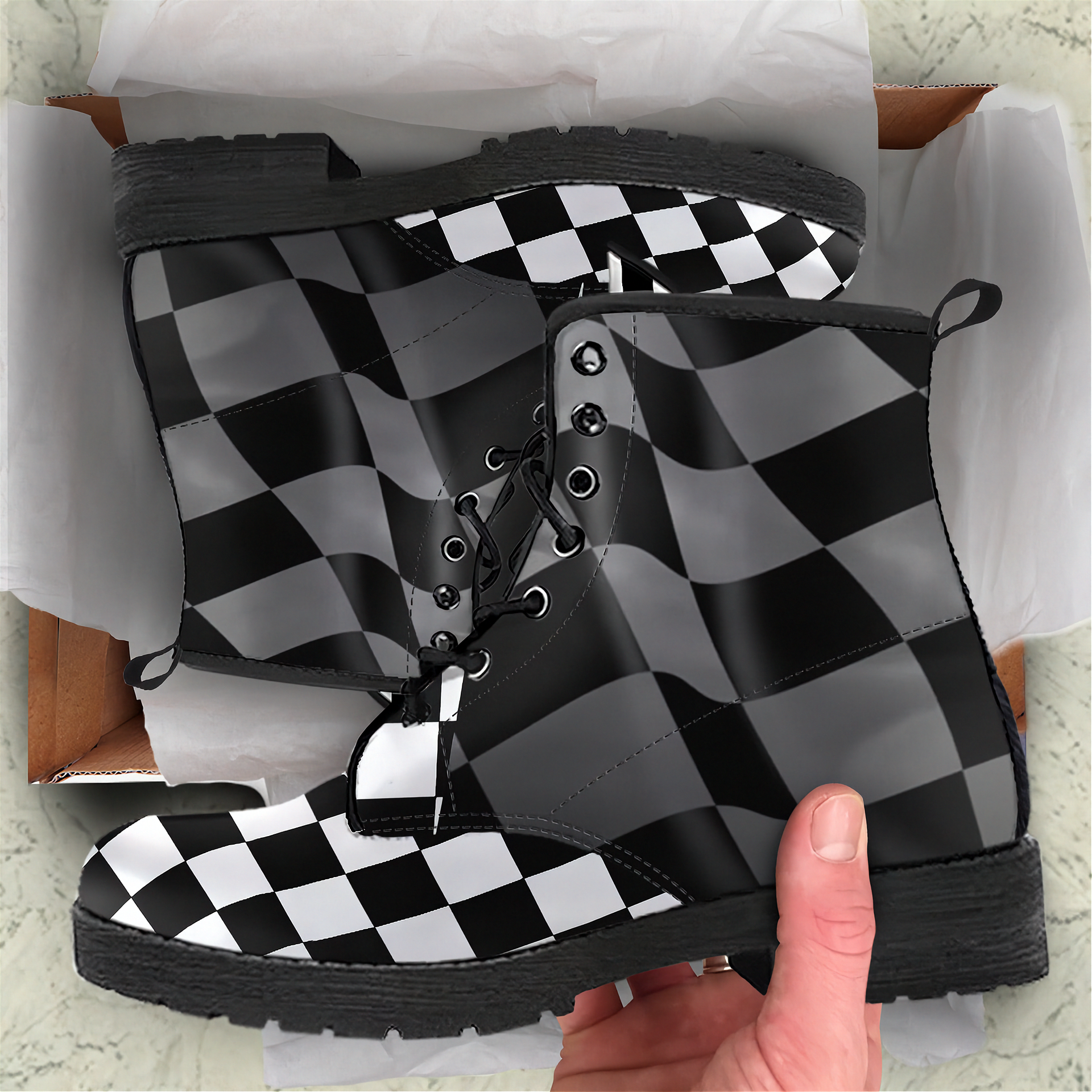 Black and white checkered boots in a box with a hand holding one boot.