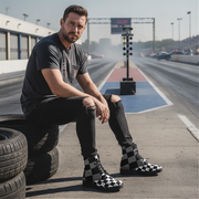 Man sitting on a tire on a race track wearing checkered boots.