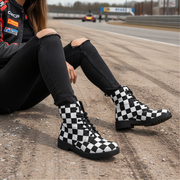Woman wearing checkered boots sitting on a race track with racing cars in the background