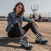 Woman wearing checkered boots sitting on a race track with cars in the background