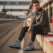 Man sitting on a race track wearing checkered boots and a leather jacket.