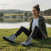 Woman sitting on grass by a lake wearing checkered boots.