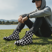 Man wearing checkered boots sitting on grass by a lake