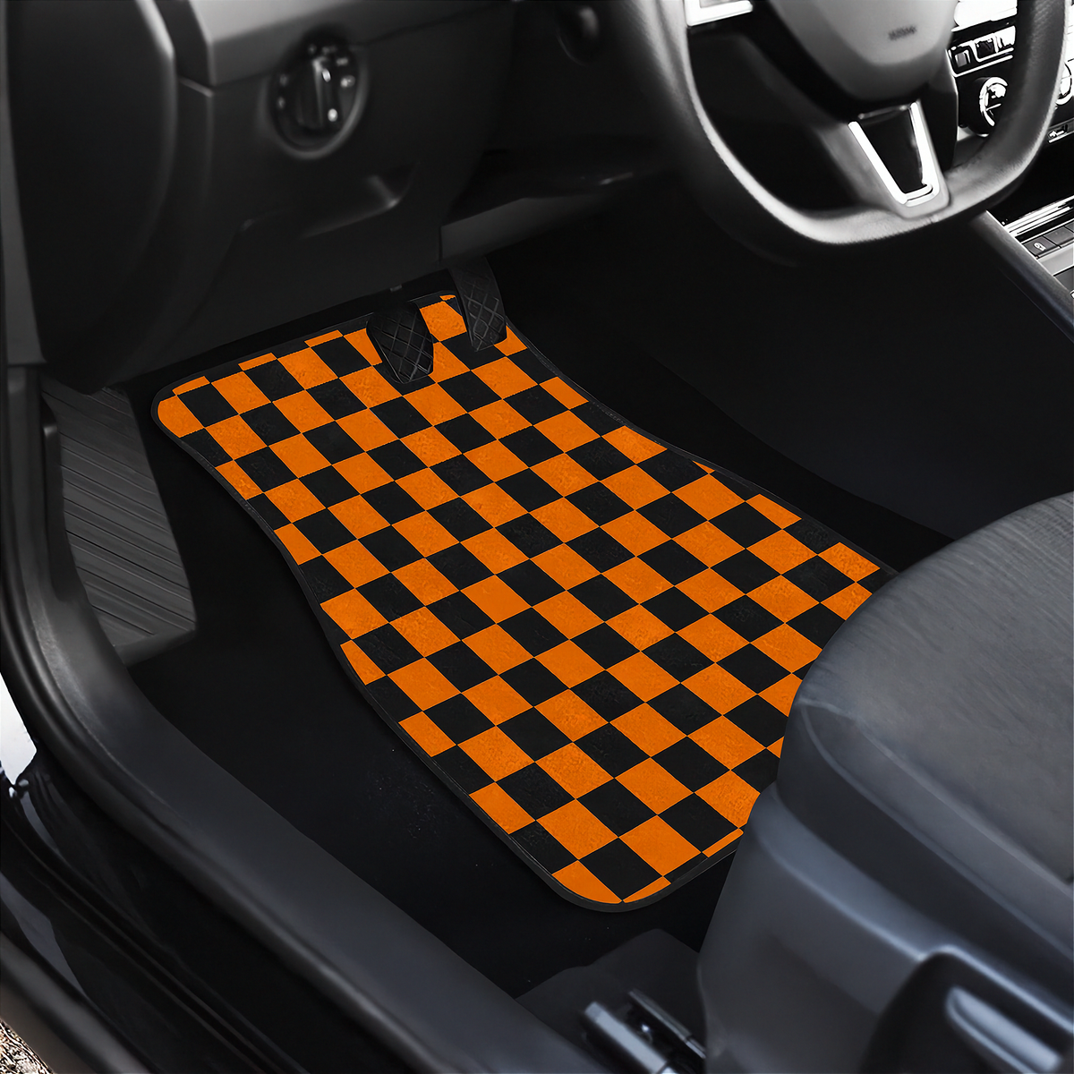 A pair of car floor mats with a bold orange and black checkerboard pattern, shown installed inside a black vehicle's driver's side footwell.
