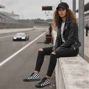 Woman wearing checkered shoes sitting on a barrier at a race track with cars in the background