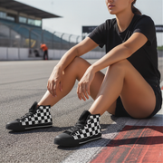 Woman wearing black and white checkered sneakers sitting on a track.