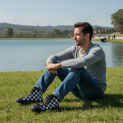 Man sitting on grass by a lake wearing checkered shoes