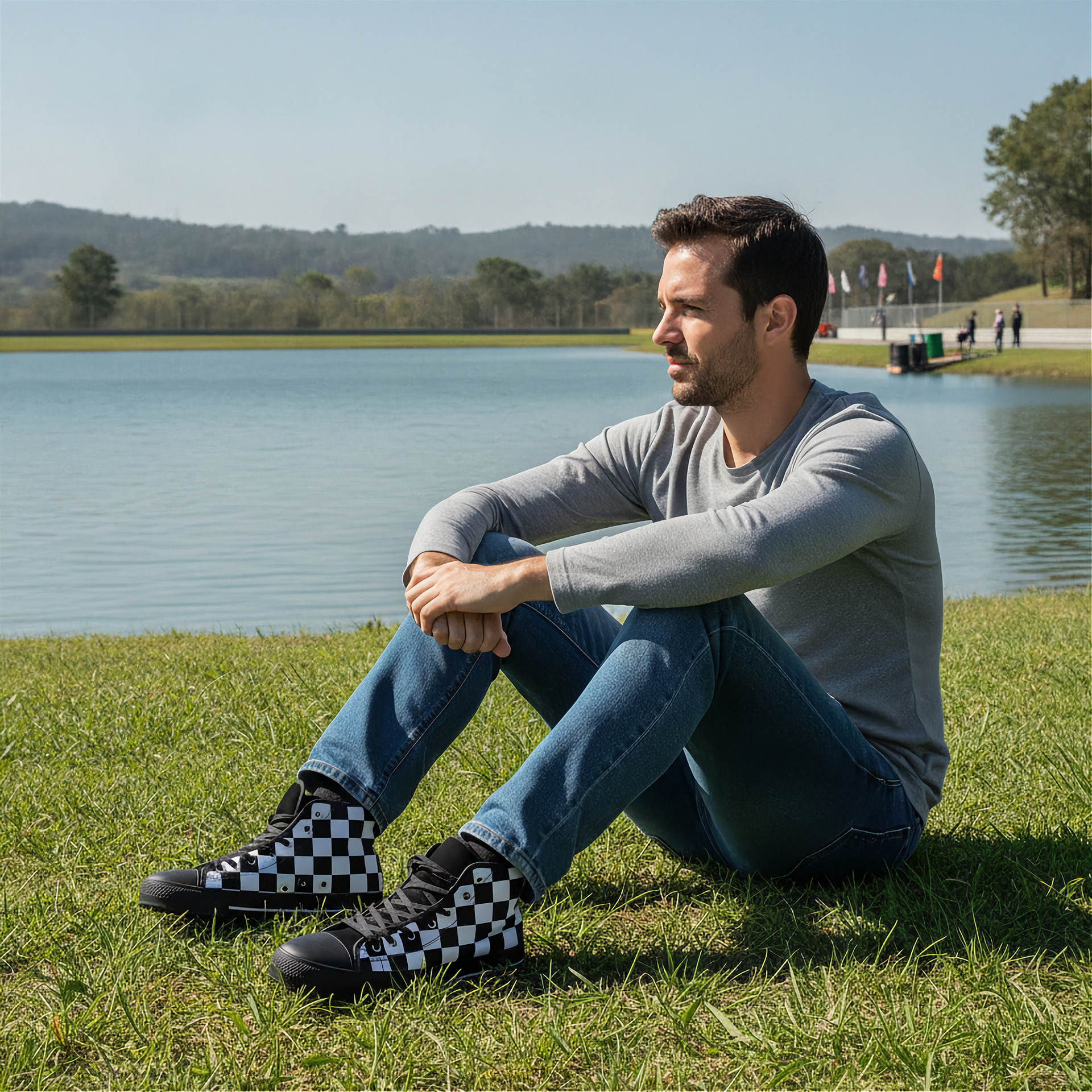 Man sitting on grass by a lake wearing checkered shoes