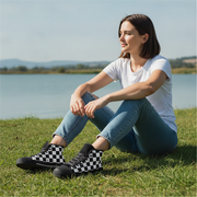 Woman sitting on grass by a lake wearing checkered shoes