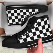 Black and white checkered sneakers in a box with a hand holding one shoe.