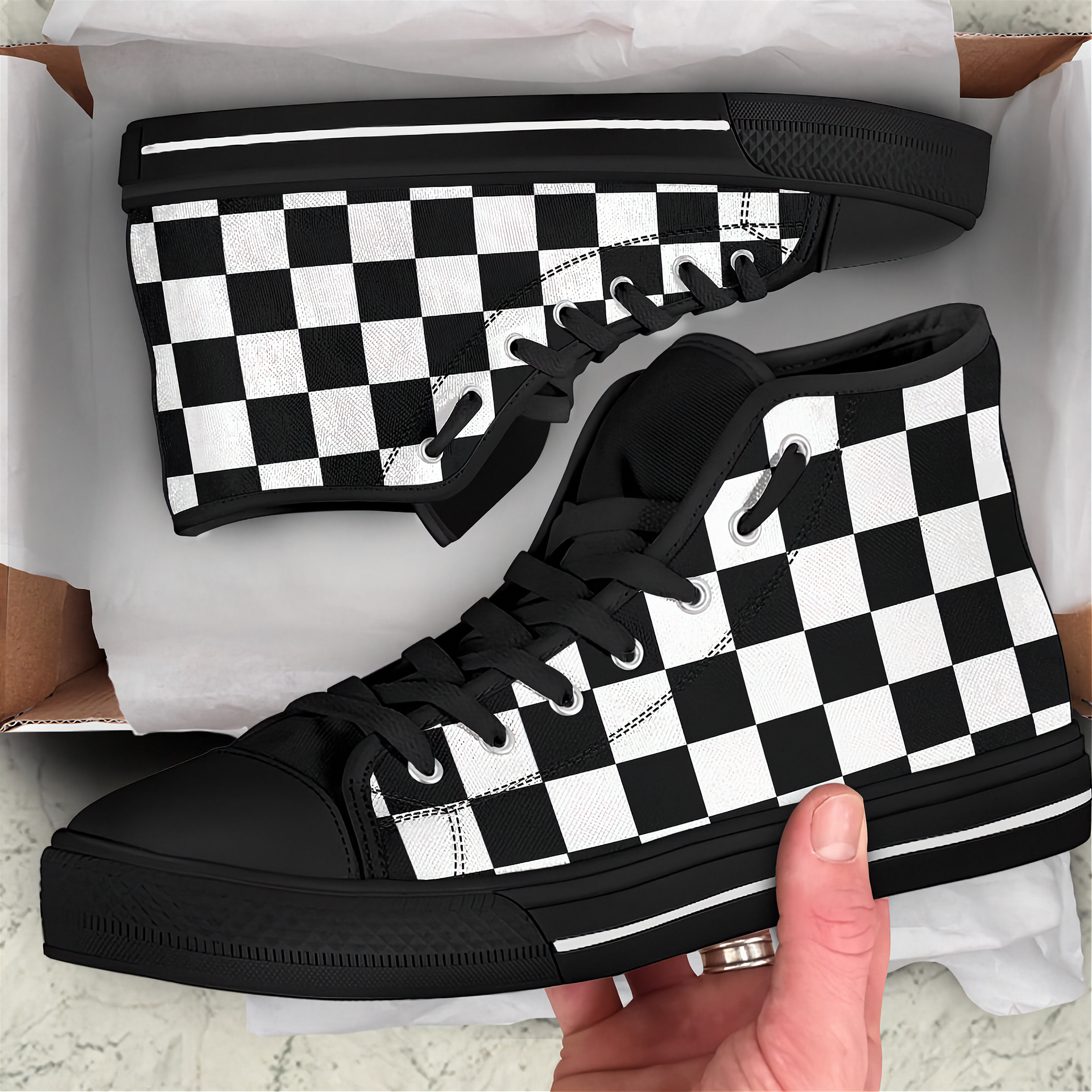 Black and white checkered sneakers in a box with a hand holding one shoe.