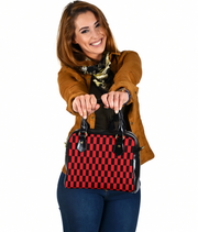 A woman wearing a brown jacket and blue jeans holds up a black handbag with a red and gold snake design against a plain white background.