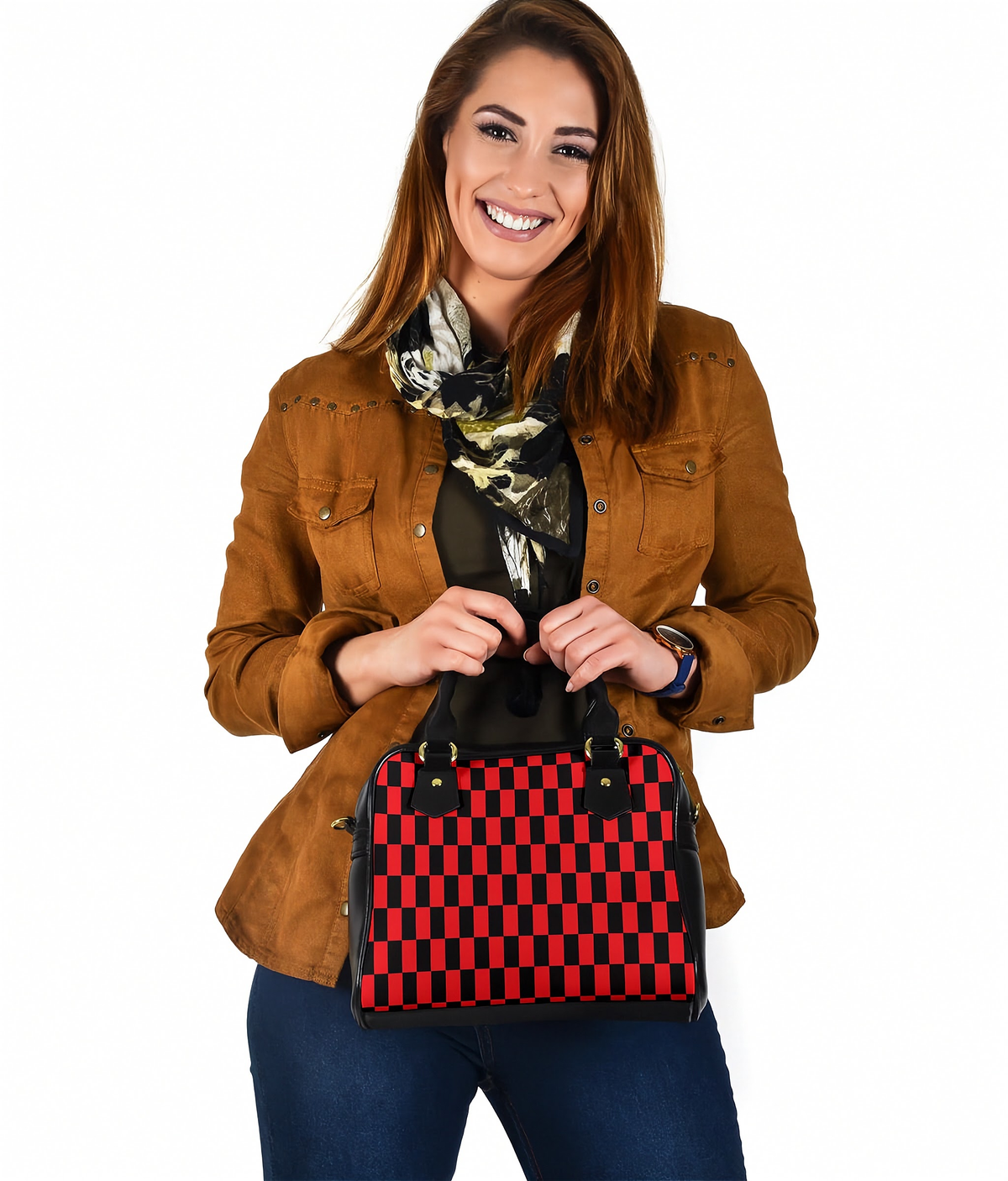 A woman wearing a brown jacket and blue jeans holds a red and black checkered handbag against a plain white background.