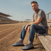 Man sitting on a wooden bench at a race track wearing checkered shoes.
