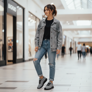 Woman in a denim jacket and jeans standing in a shopping mall.