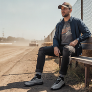 Man sitting on a bench by a race track wearing checkered boots.